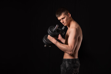 Fototapeta na wymiar young handsome muscular man doing exercises with dumbbells on a black background