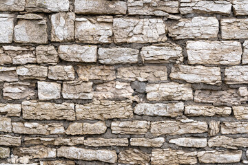 Fragment of the old fortress wall. Old blocks of gray limestone cracked and crumbled. There are traces of repair with a cement mixture. Background. Texture.