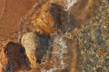 Directly Above Shot of Small Waves Rolling into Beach Dotted with Colorful Rocks and Boulders