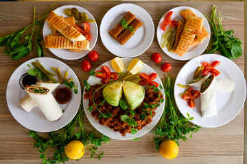 Top view of table scene with assorted take out or delivery foods. Meat and chicken doner kebab sandwich, wrap and on the plate with vegetables and sauce, including fries and pickles.