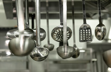 A view of several metal ladles and large mixing spoons hanging in a restaurant kitchen setting