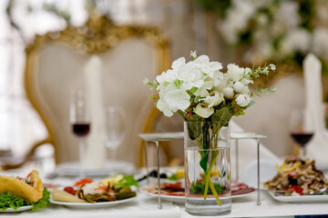 Classic and elegant artificial white decorative roses in glass full of water on wedding presidium
