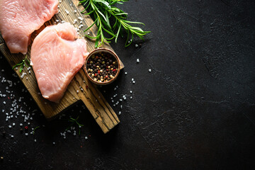 Turkey steaks with spices and herbs at wooden board at black stone table. Top view with copy space.