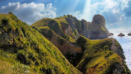 Beautiful scenic coastal coast landscape with rough rugged green rocky hills shore, blue sky morning sun rays - Karitane, New Zealand