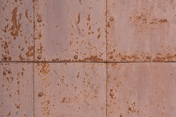 Fragment of an old fortress door covered with rectangular metal plates. Caps of powerful nails are visible. There are rust spots. Background. Texture.