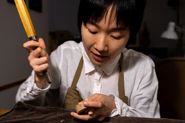 young Chinese female violin maker working with gouge to making a new violin