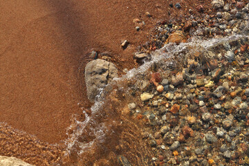 Fototapeta na wymiar Small Waves Rolling into Sandy Beach Dotted with Colorful Pebbles, Rocks, and Stones