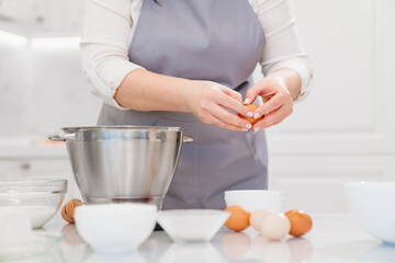 Obraz na płótnie Canvas A woman breaks an egg to prepare cream or dough in a mixer bowl.
