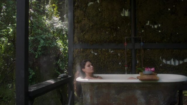 A girl in a bathtub in a forest during the rain. Beautiful young woman relaxing in the bathroom in the tropical rainforest jungle in a luxury spa while raining