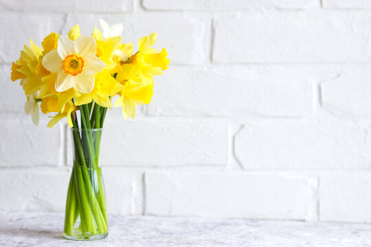 Bouquet of yellow daffodils in a vase against a brick wall. Flower arrangement. Greeting card for the holidays. Minimalism