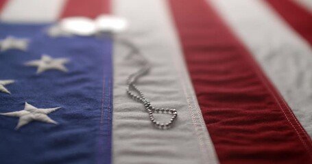 Slow motion of a US American flag with shiny military dog tags. Background for Armed Forces Day, Memorial Day, Veteran's Day, 4th of July, or other patriotic USA holiday.