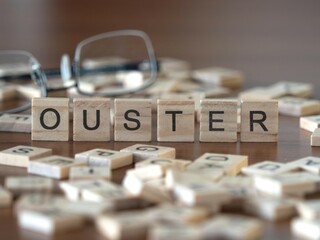 ouster word or concept represented by wooden letter tiles on a wooden table with glasses and a book