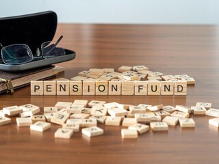 pension fund word or concept represented by wooden letter tiles on a wooden table with glasses and a book - obrazy, fototapety, plakaty