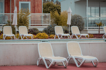 Multitude of empty deck chairs with nobody sitting on them at a fancy resort with visible modern summer cottages in the background.
