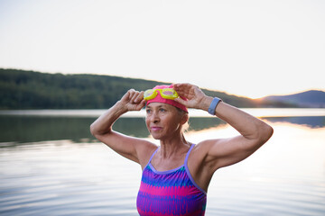 Portrait of active senior woman swimmer outdoors by lake. - Powered by Adobe