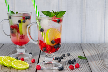 Fresh homemade summer cocktails with ice, lime and berries in glasses with a straw, copyspace