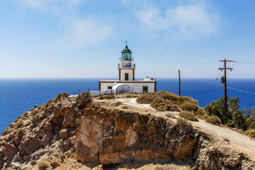 The old lighthouse on the rocky sea coast. Blue sky with clouds.