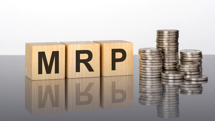 MRP - text on wooden cubes on a cold grey light background with stacks coins