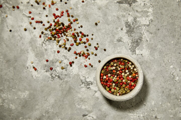 Colorful pepercorns in a gray bowl on the gray texture background. High quality photo