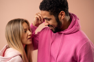 Fashion studio portrait of a happy young couple in hoodie posing over pink background.