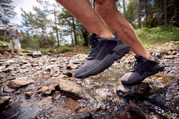 Close-up of man's legs while crossing a creek during a hiking. Hiking, nature, relationship, together