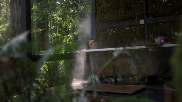 A girl in a bathtub in a forest during the rain. Beautiful young woman relaxing in the bathroom in the tropical rainforest jungle in a luxury spa while raining