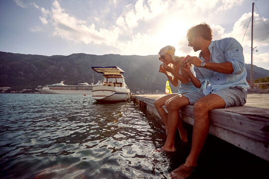 A young couple is eating juicy watermelon while sitting at the dock on the seaside. Love, relationship, holiday, sea