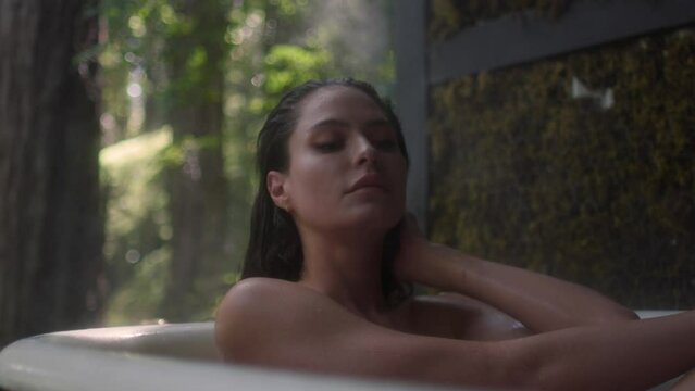 A girl in a bathtub in a forest during the rain. Beautiful young woman relaxing in the bathroom in the tropical rainforest jungle in a luxury spa while raining