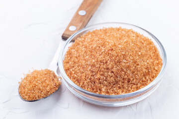 Brown sugar crystals or cane sugar in glass bowl and in spoon on white background, horizontal