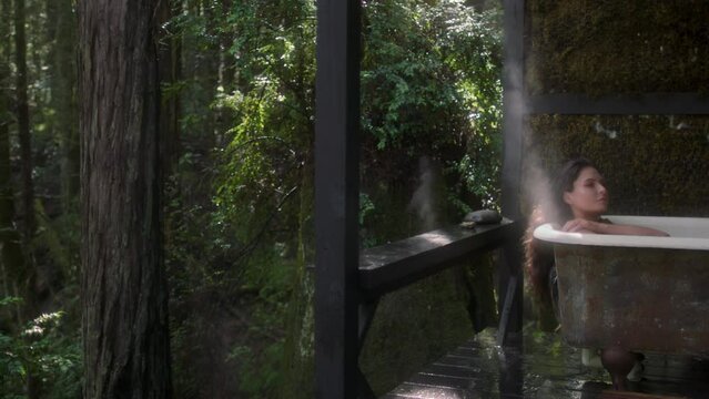 A girl in a bathtub in a forest during the rain. Beautiful young woman relaxing in the bathroom in the tropical rainforest jungle in a luxury spa while raining