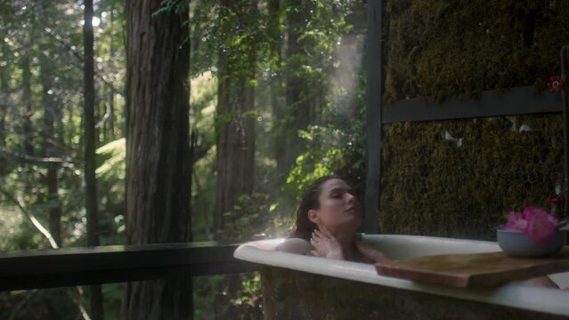 A girl in a bathtub in a forest during the rain. Beautiful young woman relaxing in the bathroom in the tropical rainforest jungle in a luxury spa while raining