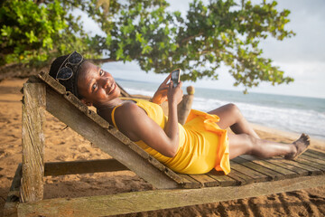 A girl relaxes on a tropical beach in africa, she is lying on a sunbed and using her smartphone.
