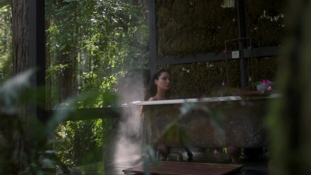 A girl in a bathtub in a forest during the rain. Beautiful young woman relaxing in the bathroom in the tropical rainforest jungle in a luxury spa while raining
