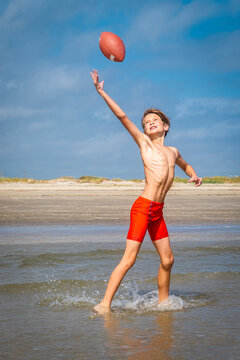 Young boy on the beach running fast to catch a football