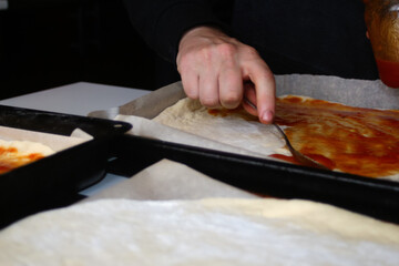 Defocus male hand make pizza dough with red tomato sauce. Homemade italian pizza. Base of Margarita. Home culinary. Man cooking and spreads the sauce by spoon. Out of focus