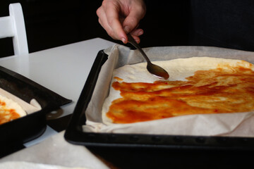 Defocus male hand make pizza dough with red tomato sauce. Homemade italian pizza. Base of Margarita. Home culinary. Men cooking and spreads the sauce by spoon. Out of focus