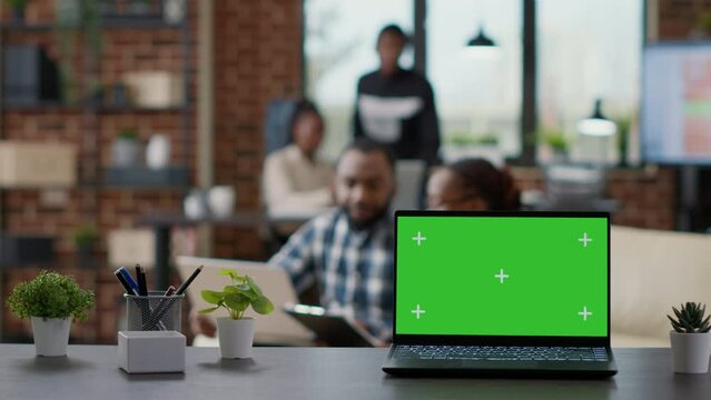 Office desk with green screen on laptop computer in workplace, mockup template with isolated chroma key and blank copypace background showed on display. Business preople with technology.