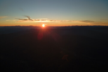 Aerial view of dark mountain hills with bright sunrays of setting sun at sunset. Hazy peaks and misty valleys in evening