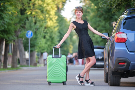 Happy young woman with suitcase bag standing near her car during road trip. Travelling and vacations concept