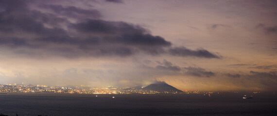Dramatic clouds over coastal city and hill at night