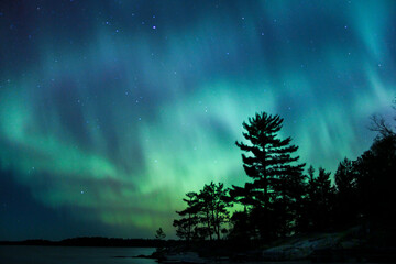 Northern lights erupt over a lake in Minnesota in a dark sky overhead shining rainbow of light