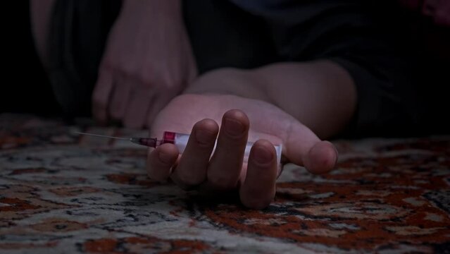 Addict's hand with syringe falls to floor just pricked heroin drugs. Slow Motion. Overdose, meth syringe falls out of weakened hand of die junkie. Social degradation, self-destruction, narcomaniac. 4K