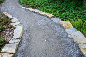 Gravel path lined by stone, an invitation to explore a woodland garden
