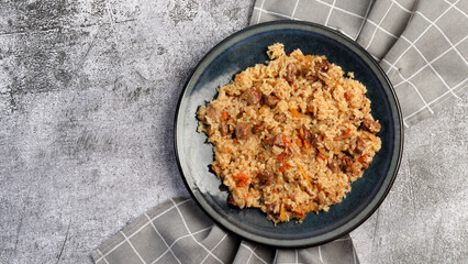Homemade pilaf with rice, meat, carrots and onions on a round plate on a dark gray background. Top view, flat lay
