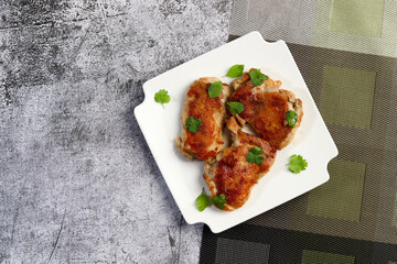 Crispy skin chicken Tapaka thighs with herbs on a white square  plate on a dark background. Top view, flat lay