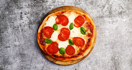 Homemade Pizza margherita with tomatoes, basil and cheese on a round wooden cutting board on a dark grey background. Top view, flat lay