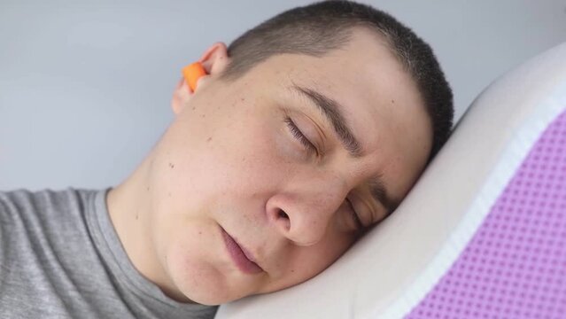 The man puts on earplugs. Close-up of an orange noise barrier. Deep sleep. The ENT doctor advises orange earmuffs to reduce ambient noise. Increased sensitivity to sounds.