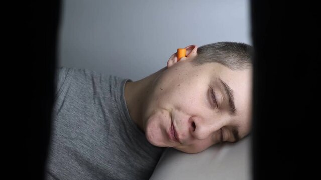 The man puts on earplugs. Close-up of an orange noise barrier. Deep sleep. The ENT doctor advises orange earmuffs to reduce ambient noise. Increased sensitivity to sounds.