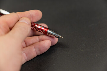 A close-up of a man's hand holding a red pen against a black background. A mature businessman with...