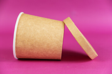 Empty cylindrical paper container with lid opposite-colored background. Brown food container for soup, ice cream, noodles, or other food.